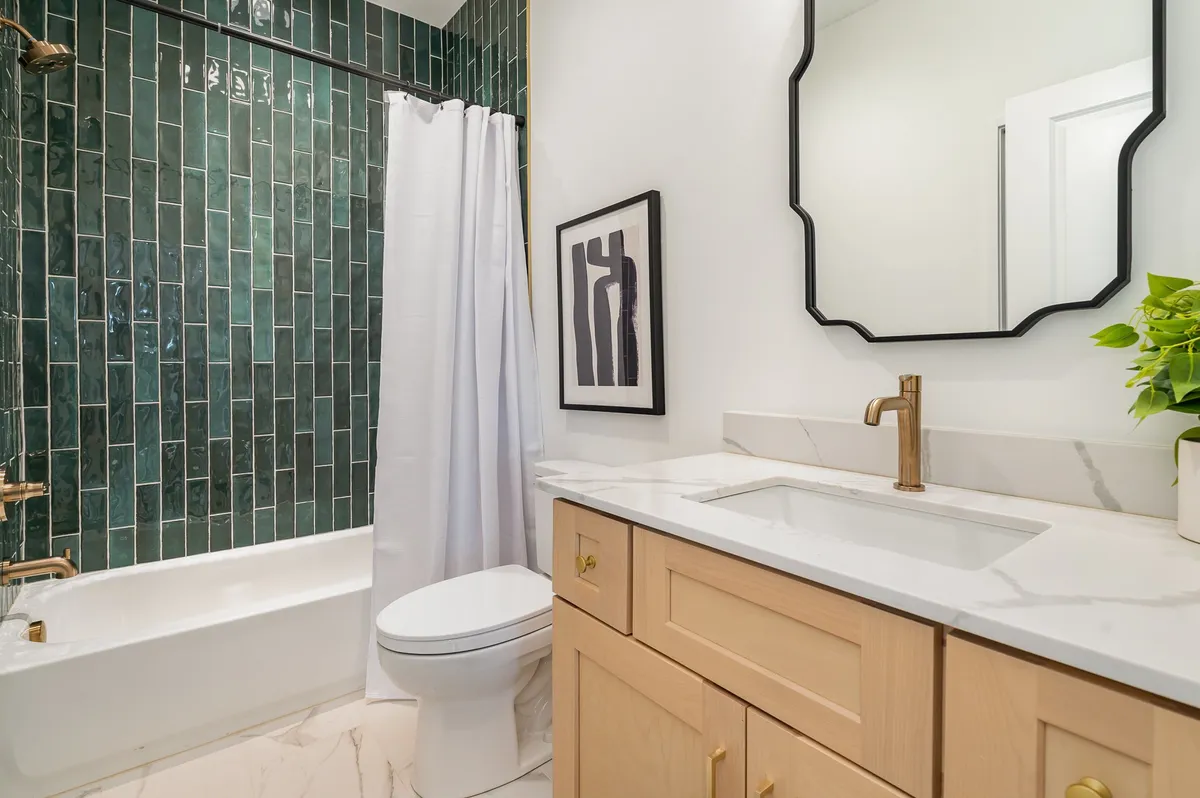 A modern bathroom with a striking green tiled wall, white soaking bathtub, gold fixtures, and a stylish vanity. Artistic details and natural light create a spa-like, inviting retreat for relaxation and rejuvenation.