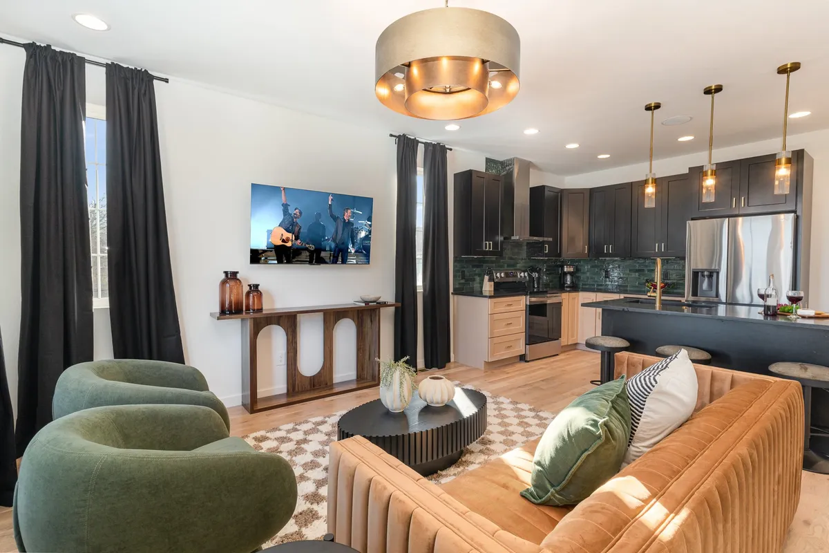 This image presents an expansive open-concept living area that seamlessly blends a plush sofa, smart TV, a modern kitchen island, and a dining table—all within one cohesive, thoughtfully arranged space. The area is bright and welcoming, ideal for group gatherings, watching movies, and shared meals.