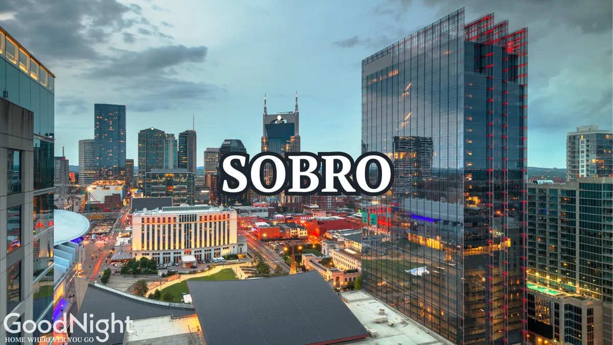 This image offers a sweeping view of the Nashville skyline at sunset, with illuminated buildings and the prominent 'SOBRO' sign in the foreground. The warm glow of the city lights and the dynamic perspective evoke a sense of energy and celebration.