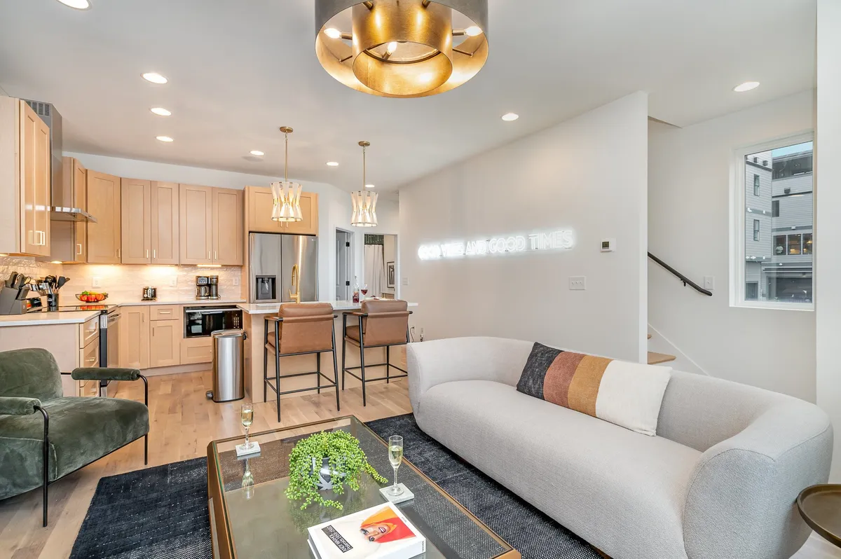 A warm and modern space that blends a comfy sofa, central kitchen island, striking light fixtures, and decorative wall art. The setup is designed for both intimate conversations and lively gatherings, making it a flexible environment for different entertaining needs.