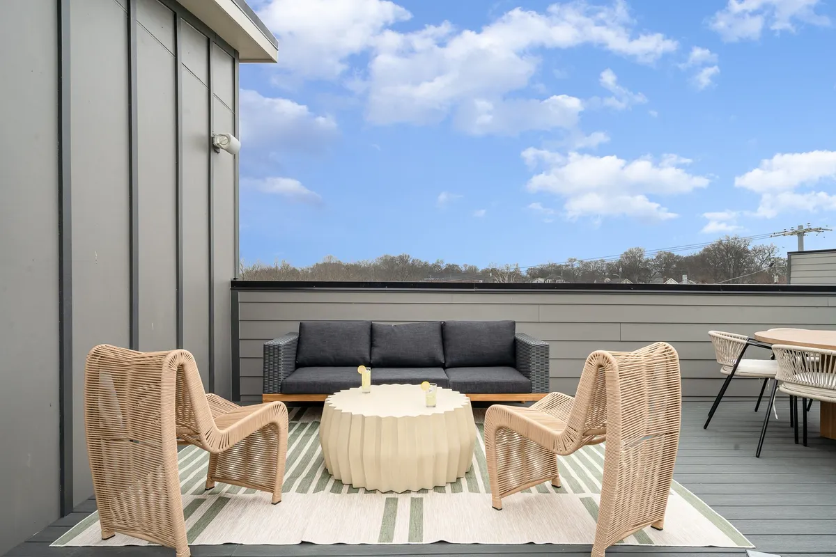An inviting outdoor lounge space with wicker chairs, a round coffee table, a sofa, and a cozy outdoor rug, all arranged for relaxation and socializing under the open sky.