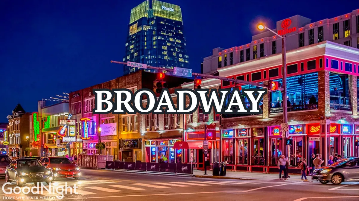 A lively street scene in downtown Nashville illuminated by neon signs, with a bustling crowd and tall buildings in the background. The energy of nightlife, live music venues, and unique dining spots is apparent.