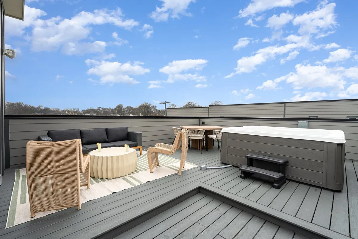 This image shows a spacious rooftop patio with a bubbling hot tub, ample outdoor seating, a coffee table, and a dining table. The arrangement suggests a perfect spot for relaxing in the hot tub or enjoying meals with friends while taking in the city views.