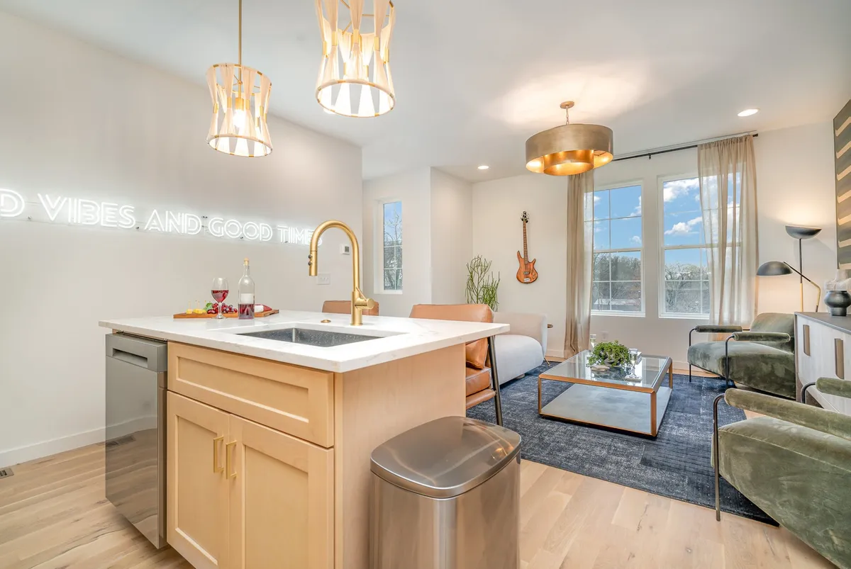 An inviting open-concept space with a kitchen island, neon sign, guitar, and comfortable living area seating. The layout encourages cooking, entertaining, and group celebrations, with modern finishes and creative touches reflecting the property’s urban edge.