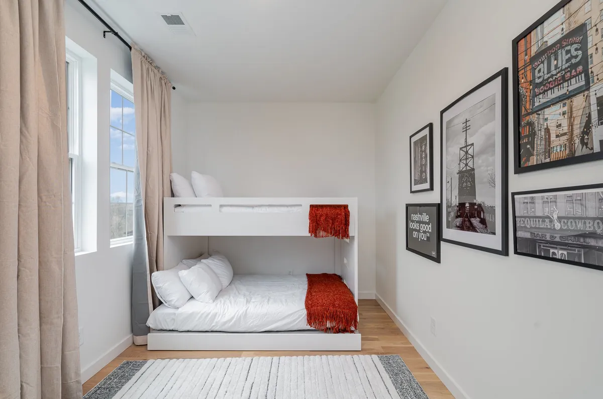 A cozy bunk bedroom with a twin-over-full bunk bed, framed artwork, and a window with curtains. The room feels playful and comfortable, ideal for younger guests or groups seeking flexible sleeping arrangements.