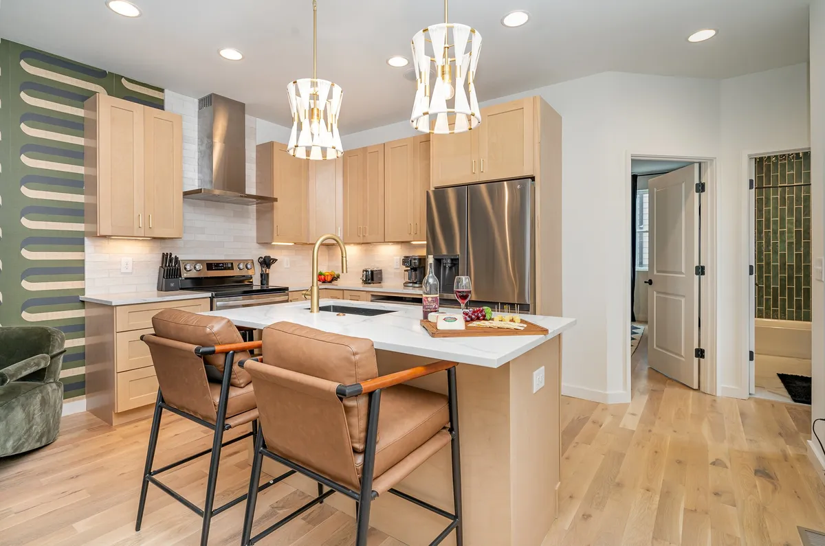 A modern kitchen is showcased here, featuring a spacious kitchen island, stylish lighting, stainless steel appliances, and a bold green accent wall. The design is open and inviting, perfect for group cooking sessions and casual dining.